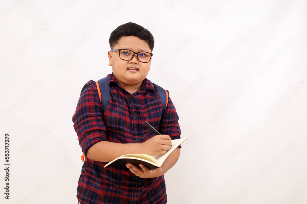 Asian school boy standing while writing something on his book. Isolated ...