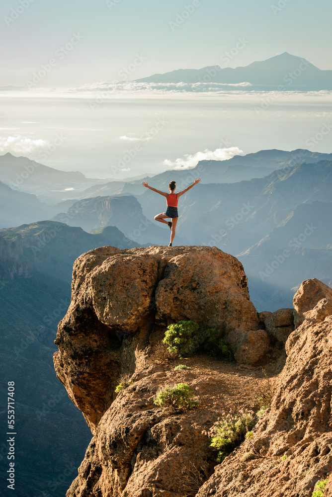 Young girl standing on a rock with the amazing view of Roque Nublo natural park and Mount Teide in the background, Gran Canary, Canary Islands, Spain