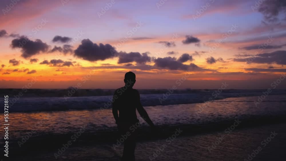 Silhouette of man walking on the beach at sunset, recreating at tropical island Bali on vacations, relaxed lifestyle. Man enjoys a beautiful fiery sunset during an evening walk along the ocean, 4k Silhouette of man walking on the beach at sunset, recreating at tropical island Bali on vacations, relaxed lifestyle. Man enjoys a beautiful fiery sunset during an evening walk along the ocean, 4k