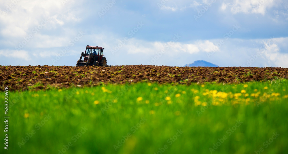 Fototapeta premium Green grass field and old small tractor plowing in the rural area of Transylvania, Romania.
