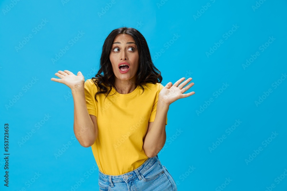 Woman in yellow t-shirt on blue background posing gestures emotions and signals with smile, hands up happiness copy space Woman in yellow t-shirt on blue background posing gestures emotions and signals with smile, hands up happiness copy space