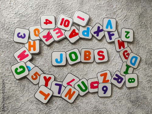 Colorful magnetic plastics with text "JOBS" around the alphabet on gray textured background. Selective focus image
