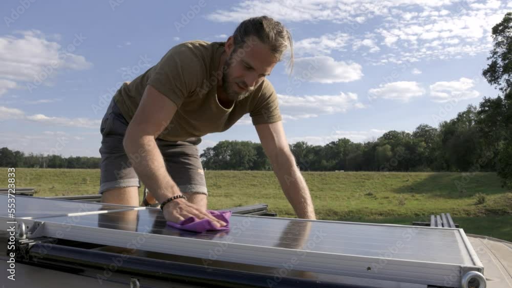 Man cleaning the solar panel on top of a camper van Man cleaning the solar panel on top of a camper van