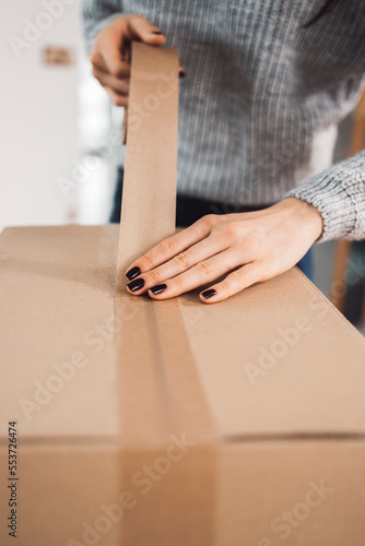 Woman hands with black nails using recycled paper tape to seal the cardboard box © VisualProduction