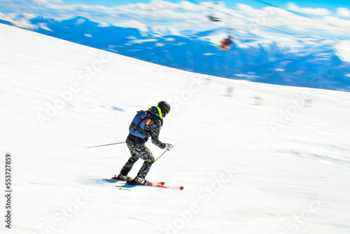 Dynamic picture of a skier on the piste in Alps. Woman skier in the soft snow. Active winter holidays, skiing downhill in sunny day. Intentional blur filter effect