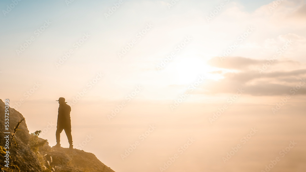 A man walking on the rock in the fog. Silhouetted man walking on the rock with fog and sunrise. Young man walking on the top of mountain. A silhouetted man in foggy weather and climbing on the rock.