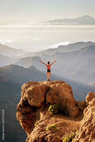 Young hiker standing on a rock overlooking the stunning views of Nublo Rural Park and Mount Teide in the distance, Tejeda, Gran Canaria, Canary Islands, Spain	