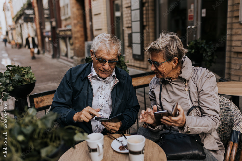 Senior couple using phones in sidewalk cafe Senior couple using phones in sidewalk cafe