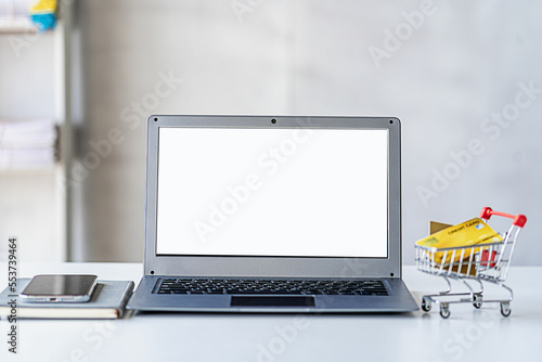 online name concept with credit card in shopping cart and laptop with white screen on wooden table online shopping photo