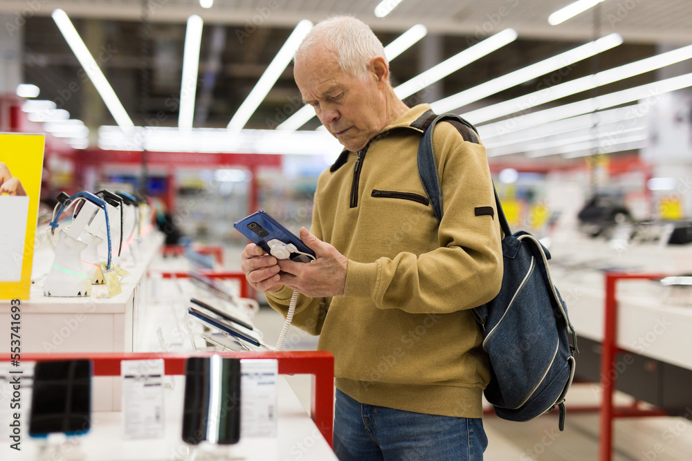 elderly man examines tablet computer in showroom of electronics store