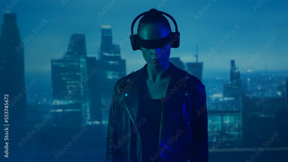 Portrait of cyberpunk girl with a smartphone in a glasses and headphones. Beautiful young woman on the background of city scyscrapers. Portrait of cyberpunk girl with a smartphone in a glasses and headphones. Beautiful young woman on the background of city scyscrapers.