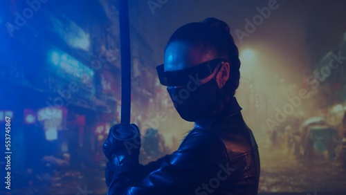 Cyberpunk ninja girl in a mask and with a katana. Beautiful female samurai woman on the background of Asian city downtown.