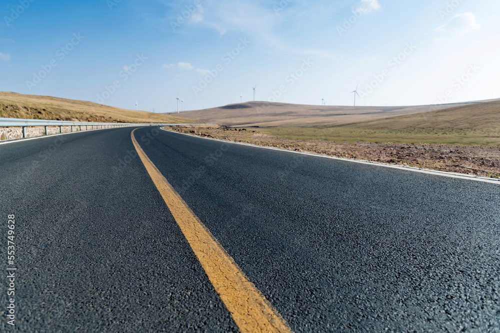 Fototapeta premium Empty asphalt highway road surrounded by fields with windmills
