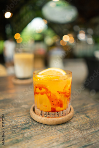 A glass of orange juice squash mixed with red strawberry syrup served with sunkist orange garnish put with blurred lamps tropical summer concept photo