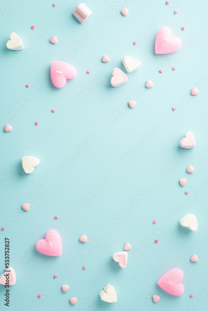 Valentine's Day concept. Top view vertical photo of heart shaped marshmallow candles and sprinkles on isolated pastel blue background with copyspace in the middle