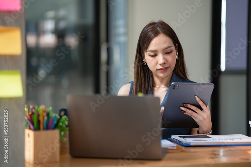 Asian businesswoman using a digital tablet while sitting at her desk in the office.