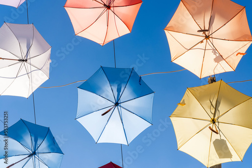 Open multi-colored umbrellas hang over passage between houses