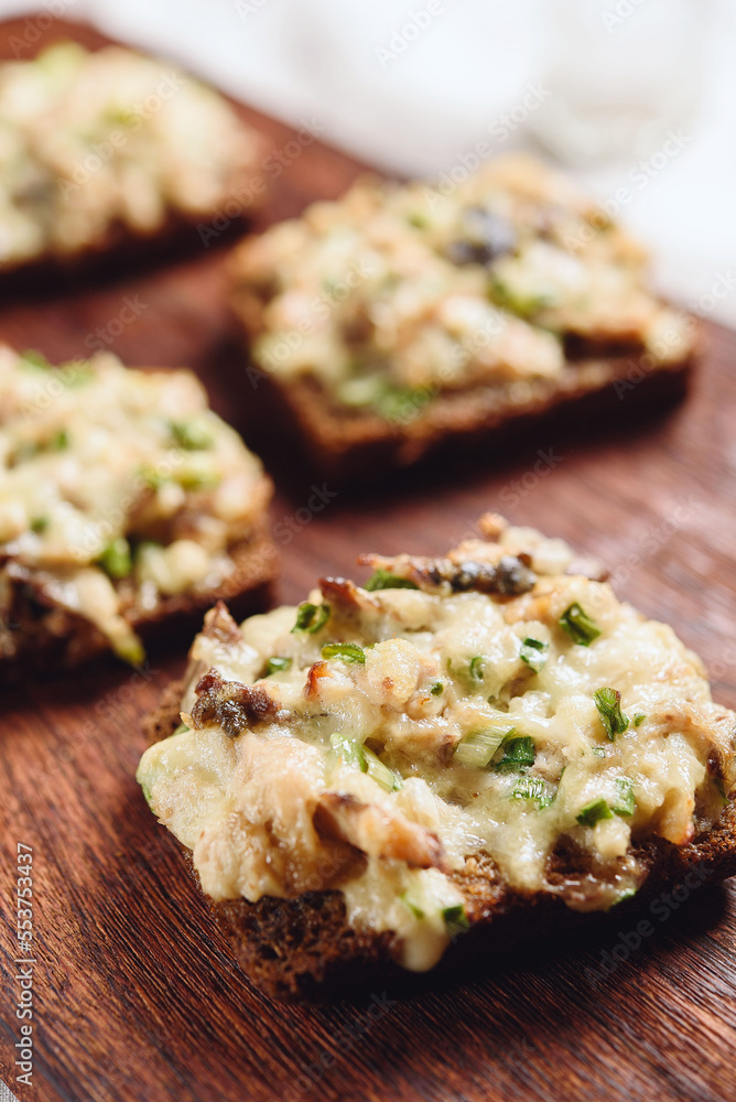 Rye bread toast with smoked mackerel, cream, cheese and green onion on wooden cutting board. Delicious appetizer, tapas. Selective focus Rye bread toast with smoked mackerel, cream, cheese and green onion on wooden cutting board. Delicious appetizer, tapas. Selective focus