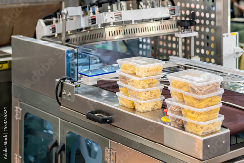 Close up food or various shape macaroni in multiple plastic box placed on automatic plastic film wrapping or protective packing machine for goods or other product etc