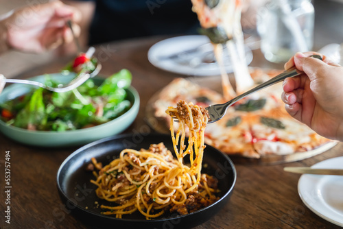 Family or friends eating food together. people eating Italian food Pasta, Pizza, Salad on the table.