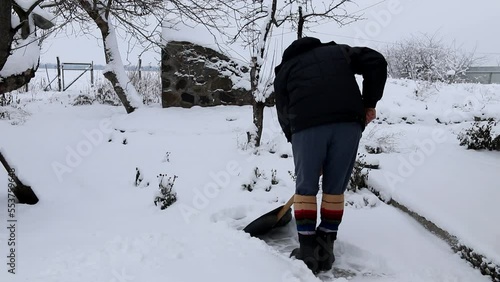 An older man removes snow from the garden path after strong snowfall