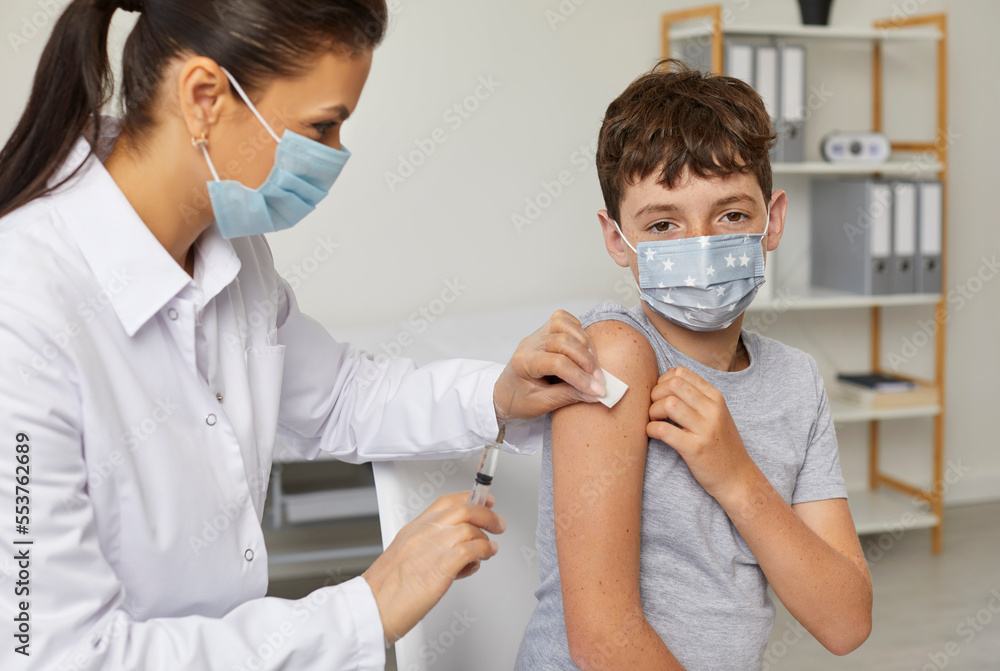 Child in facemask gets flu or Covid 19 shot at modern clinic during mass compulsory vaccination campaign. Nurse or doctor gives shoulder injection to school boy to protect him from dangerous disease