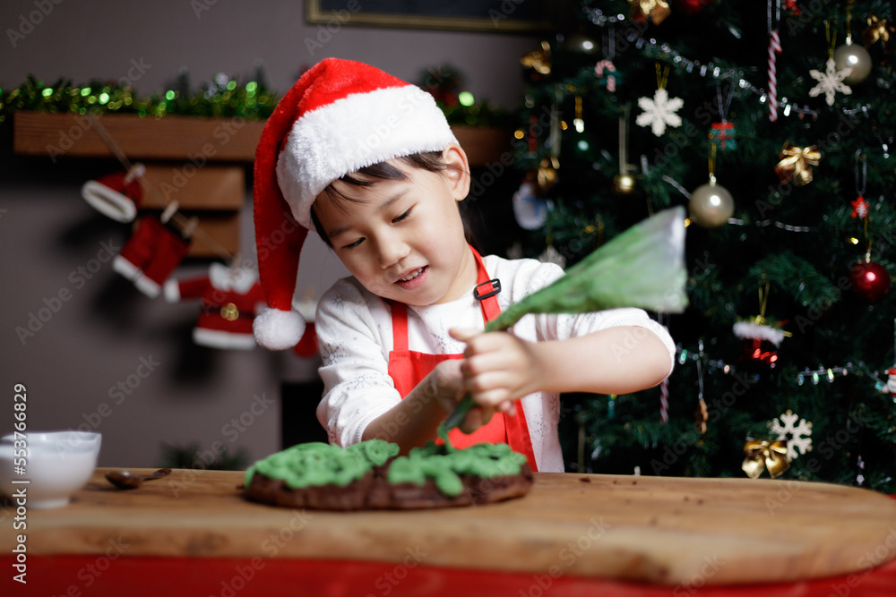 young girl wearing santa hat was preparing cake for Christmas party in front of Christmas tree at home young girl wearing santa hat was preparing cake for Christmas party in front of Christmas tree at home