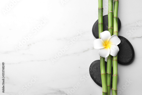 Spa stones  bamboo stems and plumeria flower on white marble table  flat lay. Space for text