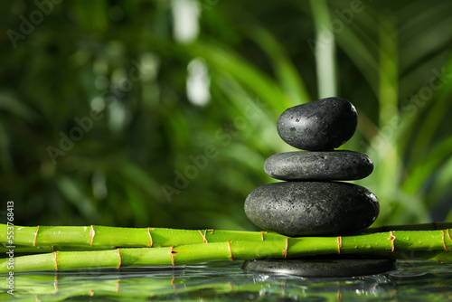 Stacked stones on bamboo stems over water against blurred background. Space for text