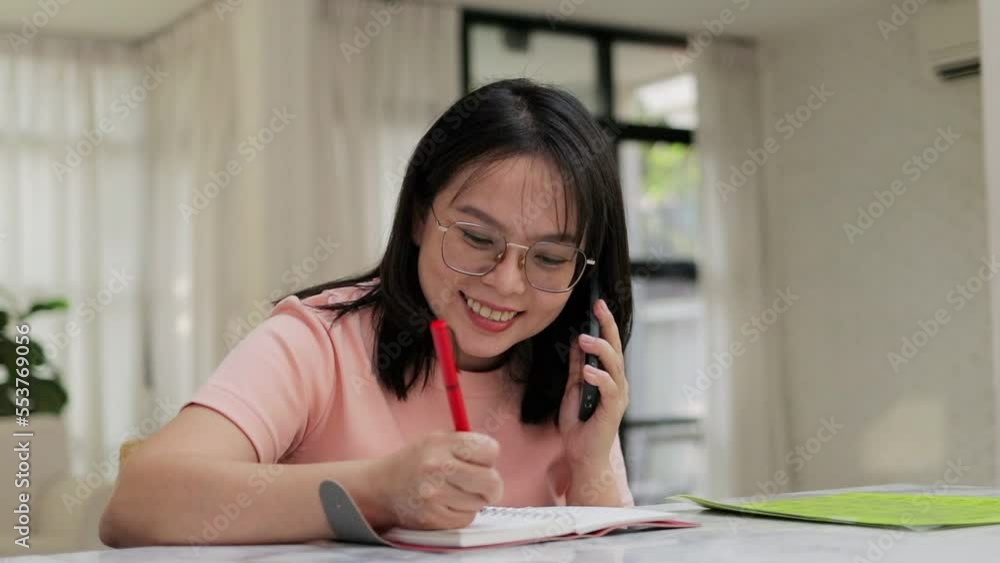 Asian woman sitting at home working Talk on the phone and jot down information in a notebook. Modern women work from home. Asian woman sitting at home working Talk on the phone and jot down information in a notebook. Modern women work from home.