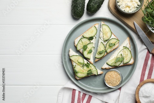 Tasty cucumber sandwiches with sesame seeds and pea microgreens on white wooden table, flat lay. Space for text
