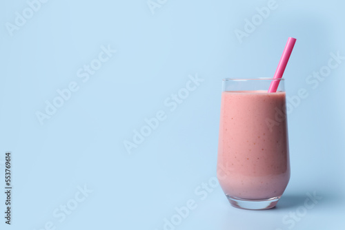 Glass with delicious berry smoothie and strawberries on light blue background. Space for text