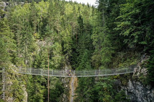 Drone photograph with hiker crossing a suspended metal bridge over a mountain gorge photo