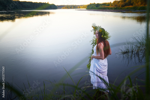 Portrait of beautiful slavic girl with long hair with flower crown in a water of river or lake on nature in warm evening. National selebration of summer holiday of Ivan Kupala photo