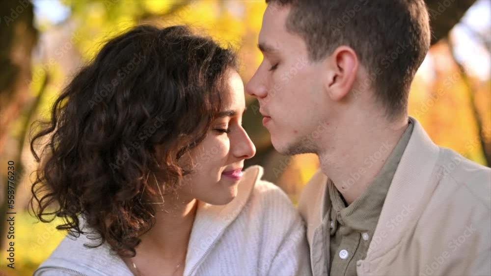 A romantic couple in an autumn park. Man kissing his woman. Autumn atmosphere, yellowed trees and leaves on background. Slow motion A romantic couple in an autumn park. Man kissing his woman. Autumn atmosphere, yellowed trees and leaves on background. Slow motion
