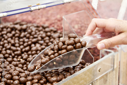Hand with scoop dragee in chocolate glaze in shop