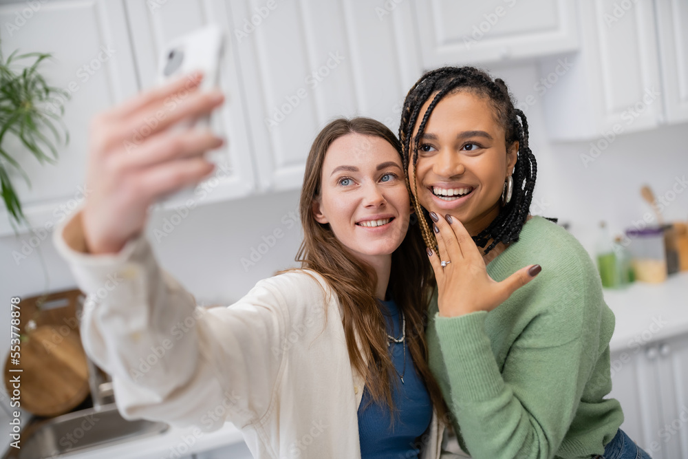 lesbian woman taking selfie while happy african american girlfriend showing engagement ring on finger. lesbian woman taking selfie while happy african american girlfriend showing engagement ring on finger.