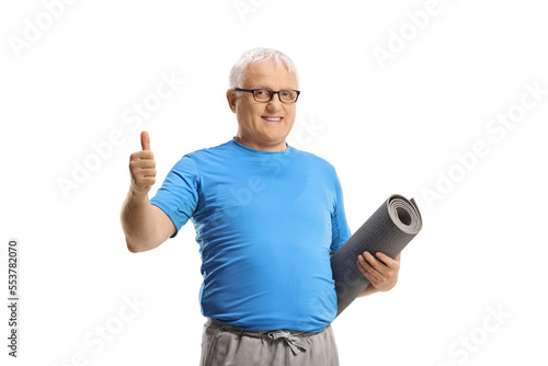 Mature man in sportswear holding an exercise mat and showing thumbs up