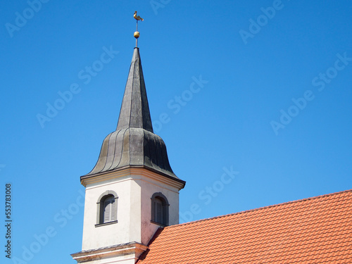 Close up view to church tower with golden rooster on the top against clean blue sky.
