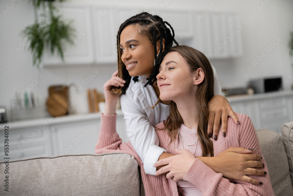 young african american lesbian woman hugging joyful girlfriend in living room. young african american lesbian woman hugging joyful girlfriend in living room.