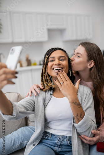 happy african american and lesbian woman showing engagement ring while taking selfie with girlfriend.