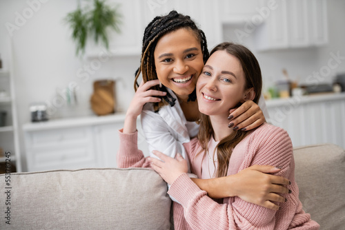 positive african american lesbian woman hugging joyful girlfriend in living room.