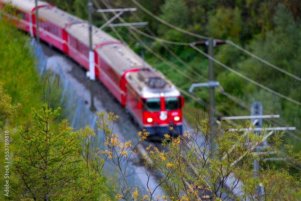 Naklejka premium Anterior Rhine valley gorge with blurry red train arriving at railway station Versam-Safien on a sunny autumn morning. Photo taken September 26th, 2022, Versam Station, Switzerland.