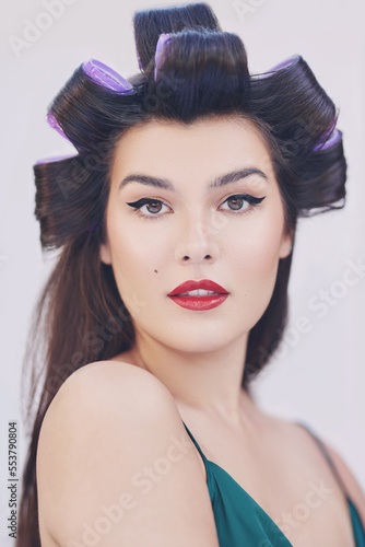 1950s styled beauty. Female model with rollers in her hair, with black flicked eyeliner and red lipstick and a beauty spot.