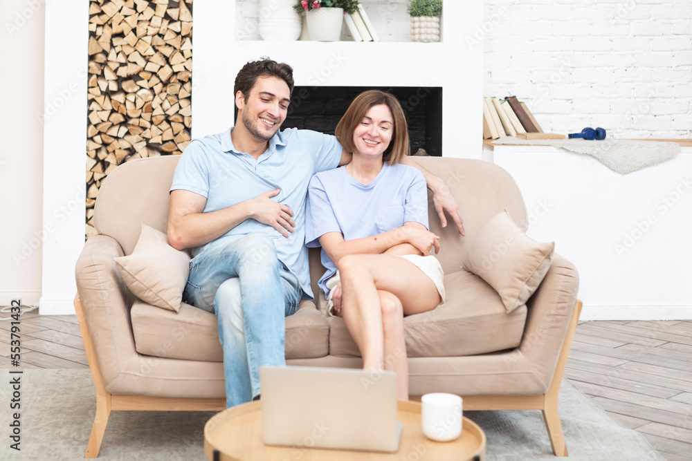 Young cheerful couple sitting on the couch in the living room and watching interesting game at laptop