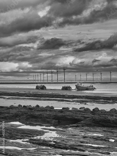 A fishing boat returns to a rugged, rock-strewn shore, recently plagued by mass marine die-offs, ahead of a wind farm on the North East English Coast.