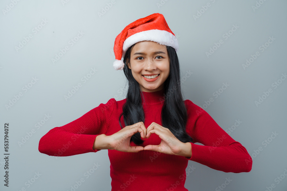 Pretty lovely lady asian thai women in red sweater and santa christmas hat isolated over grey background. heart shaped Pretty lovely lady asian thai women in red sweater and santa christmas hat isolated over grey background. heart shaped