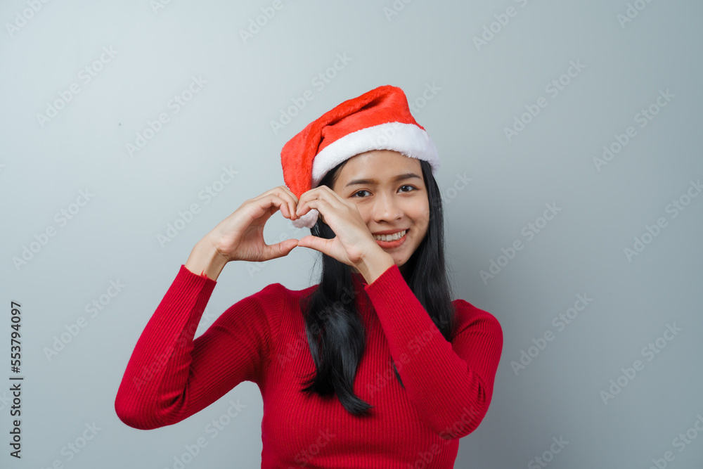 Pretty lovely lady asian thai women in red sweater and santa christmas hat isolated over grey background. heart shaped Pretty lovely lady asian thai women in red sweater and santa christmas hat isolated over grey background. heart shaped