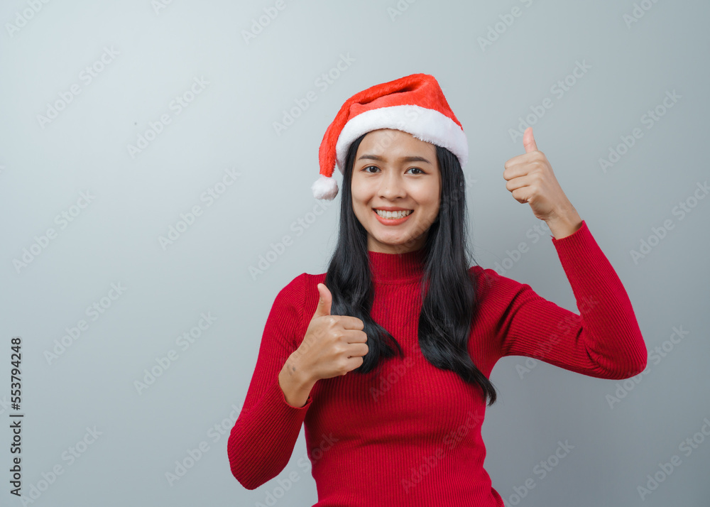 Pretty lovely lady asian thai women in red sweater and santa christmas hat isolated over grey background. thumb up Pretty lovely lady asian thai women in red sweater and santa christmas hat isolated over grey background. thumb up