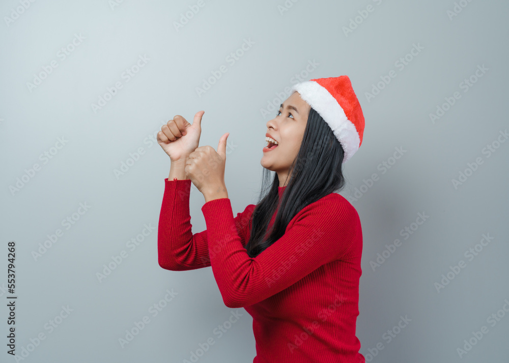 Pretty lovely lady asian thai women in red sweater and santa christmas hat isolated over grey background. thumb up Pretty lovely lady asian thai women in red sweater and santa christmas hat isolated over grey background. thumb up